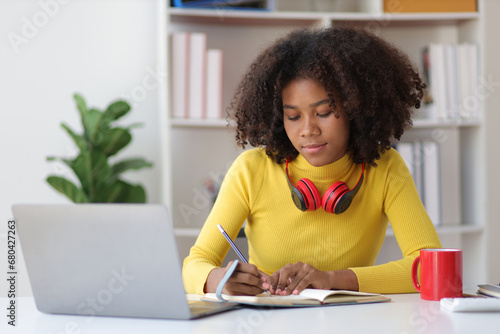 Young african woman working with laptop and reading books preparing for exams at her home.