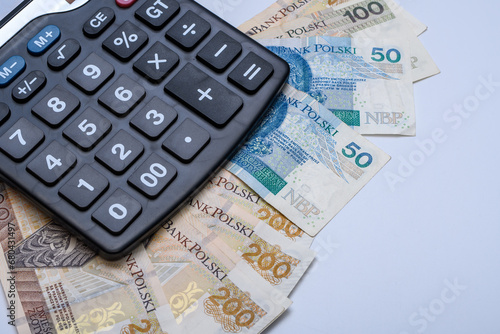 Pieniądze, polskie banknoty PLN leżą na biurku obok kalkulatora