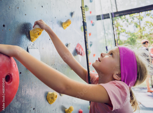 A strong baby climber climbs an artificial wall with colorful grips and ropes.