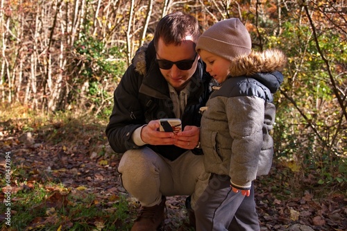 Father and his toddler using mobile phone in the forest