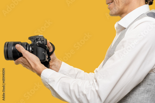 Closeup of young man with modern camera work as photographer on yellow background, he seamlessly blends the classic art of photography with the advancements of the digital age.