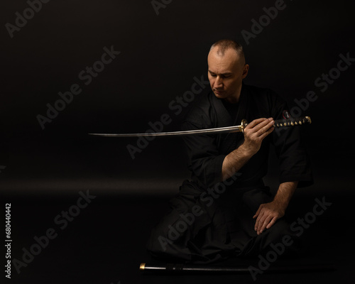 Portrait of aikido sensei master with black sensei belt in taekwondo kimono witn sword katana on black background. Traditional samurai hakama kimono.