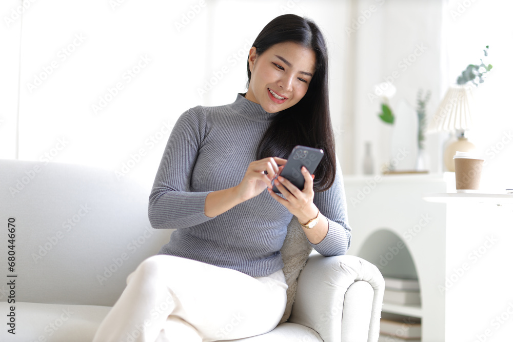 Happy young woman sitting on sofa using smartphone in living room at home. Happy young woman sitting on sofa using smartphone in living room at home.