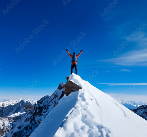 Mountaineer triumphs atop snowy peak, blue sky backdrop.  © henjon