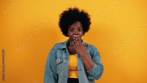 Surprised woman can not believe in luck. Excited woman with afro hairstyle closing her mouth, looking at camera with big eyes and smile shocked by sudden news. Oh my god wow. Studio isolated photo