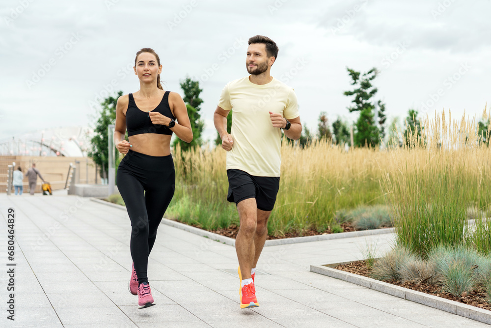 A fitness trainer and a client train together in sportswear. Uses sportswear and accessories app in smart watch, male and female runner.