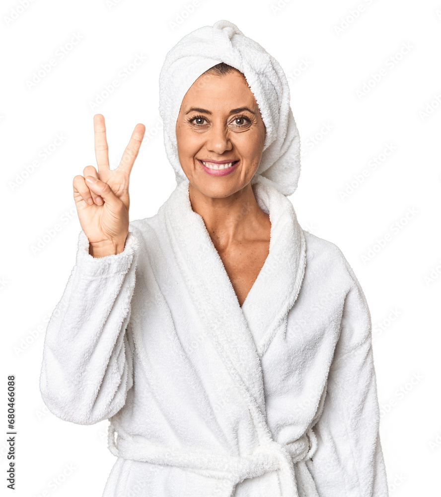 Middle-aged woman with towel post-shower in studio showing number two with fingers.