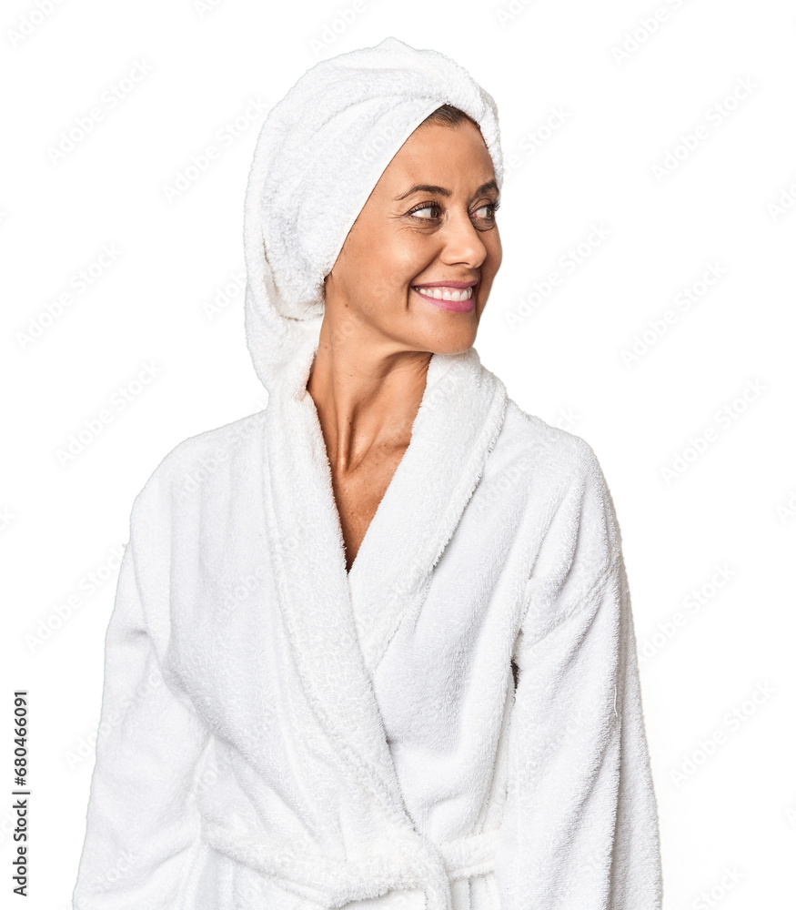 Middle-aged woman with towel post-shower in studio looks aside smiling, cheerful and pleasant.