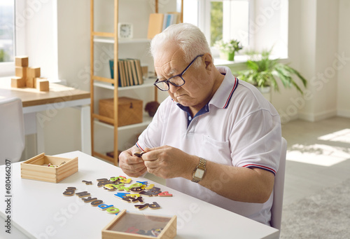 Elderly man is putting together a puzzle in a modern dementia rehabilitation center. Creative idea of memory loss training during dementia, Alzheimer's disease. The concept of human mental health.