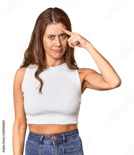 Middle-aged woman portrait in studio setting pointing temple with finger, thinking, focused on a task.