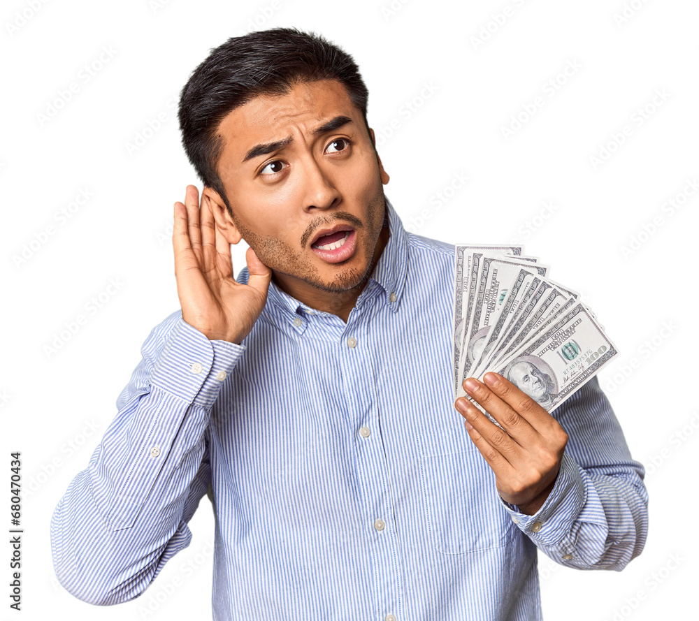 Young Chinese man holding dollar bills in studio trying to listening a gossip. Young Chinese man holding dollar bills in studio trying to listening a gossip.
