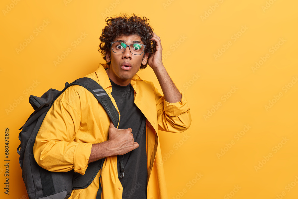 Studio sideway waist up of young fit surprised Hindu male student seeing something unusual or unexpected standing on left isolated on yellow background with blank space for your advertisement Studio sideway waist up of young fit surprised Hindu male student seeing something unusual or unexpected standing on left isolated on yellow background with blank space for your advertisement