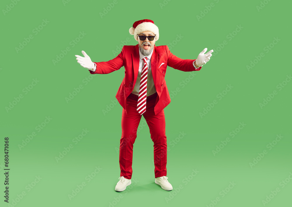 Happy man wearing christmas hat doing welcome gesture. Full length portrait of excited bearded man in red suit and cool sunglasses standing with hands spreading to sides on isolated studio background Happy man wearing christmas hat doing welcome gesture. Full length portrait of excited bearded man in red suit and cool sunglasses standing with hands spreading to sides on isolated studio background