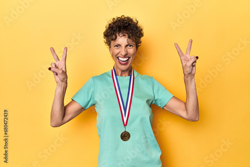 Proud sportswoman displaying her winning medal on yellow studio background photo