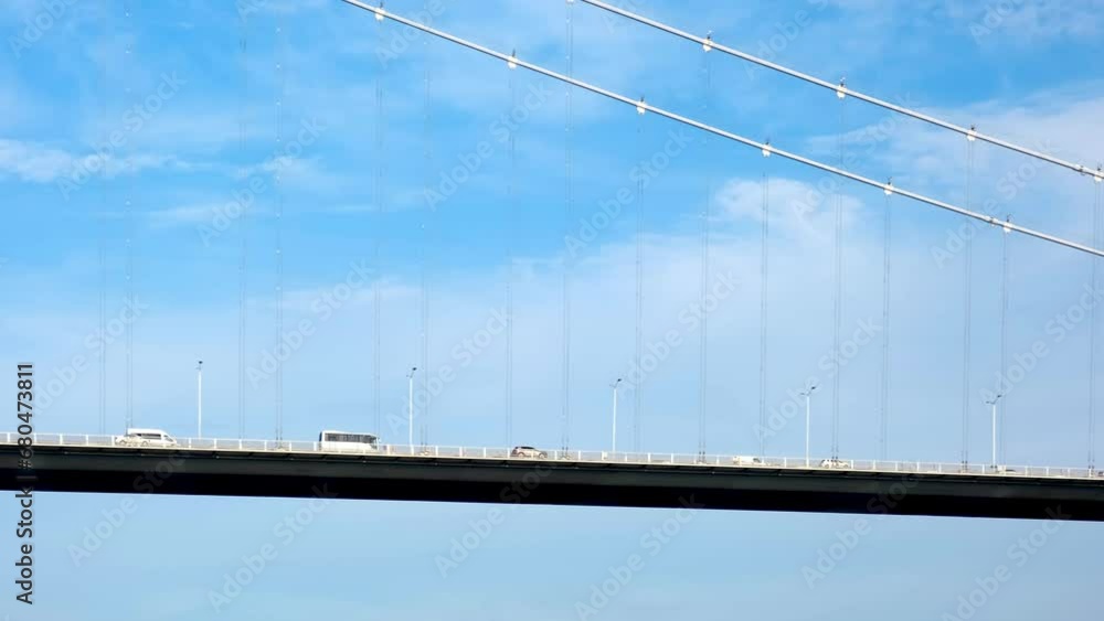The suspension bridge across the strait carries many cars, buses and trucks. Against the background of a beautiful sky with clouds. The suspension bridge across the strait carries many cars, buses and trucks. Against the background of a beautiful sky with clouds.