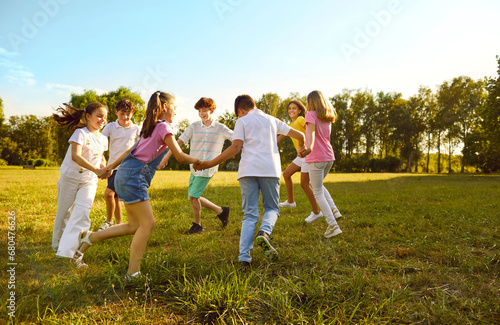 Group of a kids friends playing outside in the park standing in a circle and holding hands. Happy children playing games and having fun outdoor on a sunny summer day in casual clothes.