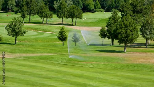 Automatic high-pressure water sprinkler at green golf course watering the grass.
