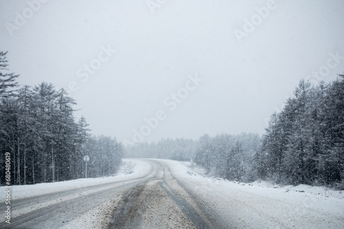 Photo of the winter road during the snowfall in Magadan, Russia. Snow showers on the trees and hills. Slush on the way. Fog and haze, low visibility due to snowstorm. Extreme weather conditions © julianeroznak
