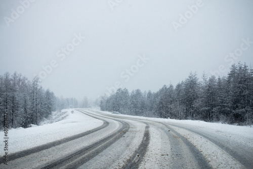 Photo of the winter road during the snowfall in Magadan, Russia. Snow showers on the trees and hills. Slush on the way. Fog and haze, low visibility due to snowstorm. Extreme weather conditions