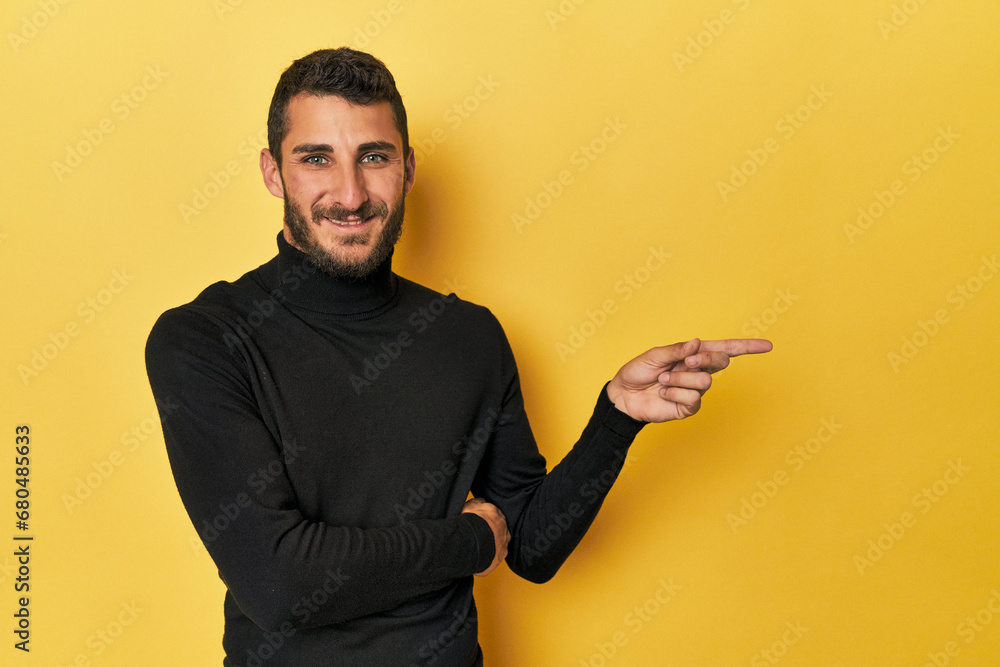 Young Hispanic man on yellow background smiling cheerfully pointing with forefinger away. Young Hispanic man on yellow background smiling cheerfully pointing with forefinger away.