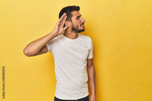 Young Hispanic man on yellow background trying to listening a gossip.