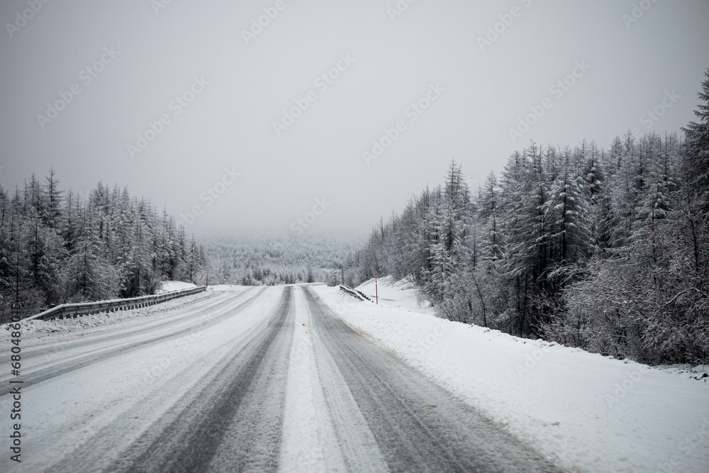 Photo of the winter road during the snowfall in Magadan, Russia. Snow showers on the trees and hills. Slush on the way. Fog and haze, low visibility due to snowstorm. Extreme weather conditions Photo of the winter road during the snowfall in Magadan, Russia. Snow showers on the trees and hills. Slush on the way. Fog and haze, low visibility due to snowstorm. Extreme weather conditions