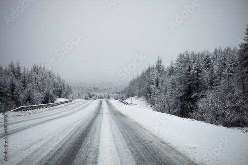 Photo of the winter road during the snowfall in Magadan, Russia. Snow showers on the trees and hills. Slush on the way. Fog and haze, low visibility due to snowstorm. Extreme weather conditions
