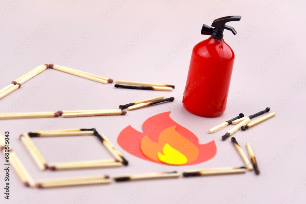 A box of matches placed next to a toy red fire extinguisher against a light background. A box of matches placed next to a toy red fire extinguisher against a light background.