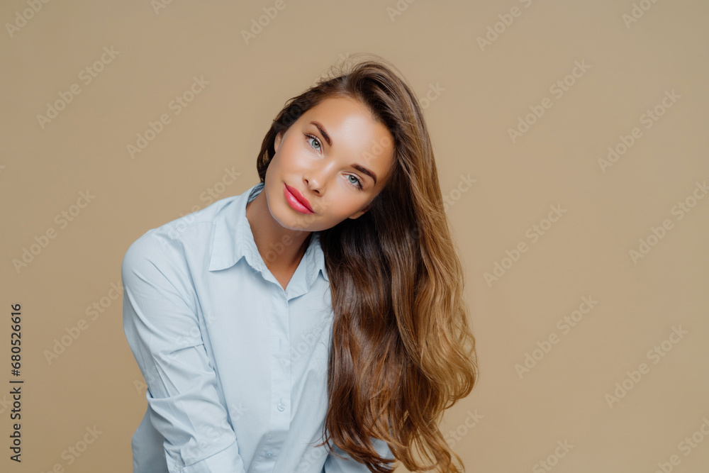 Sultry woman with voluminous hair in blue blouse tilting head on a beige background Sultry woman with voluminous hair in blue blouse tilting head on a beige background