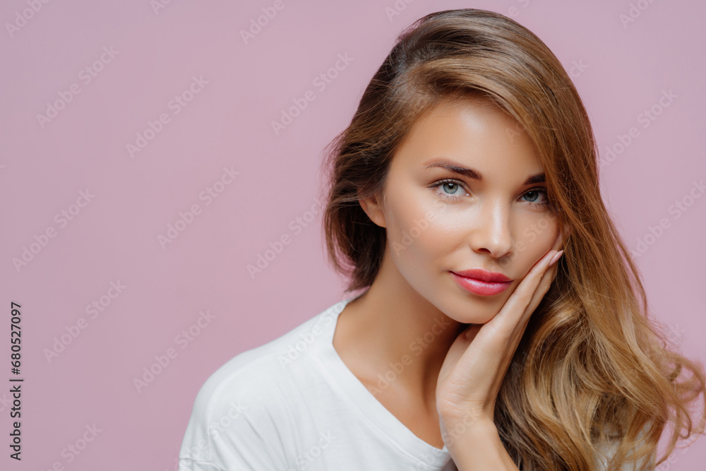 Graceful woman with hand on face, wavy hair, in a white tee, with a thoughtful expression Graceful woman with hand on face, wavy hair, in a white tee, with a thoughtful expression