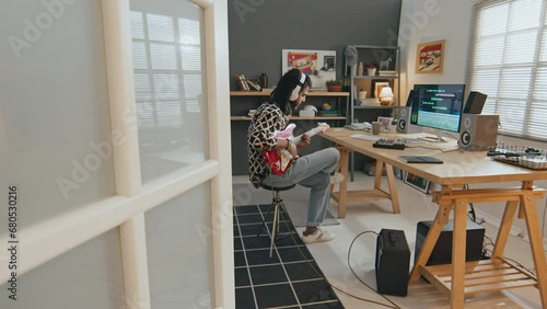Full shot of young Arab male musician in headphones sitting in living room at home, composing new song on electric guitar and recording track on computer with digital editing software photo