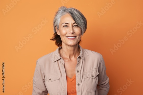 Portrait of a satisfied woman in her 50s sporting a versatile denim shirt against a pastel orange background. AI Generation