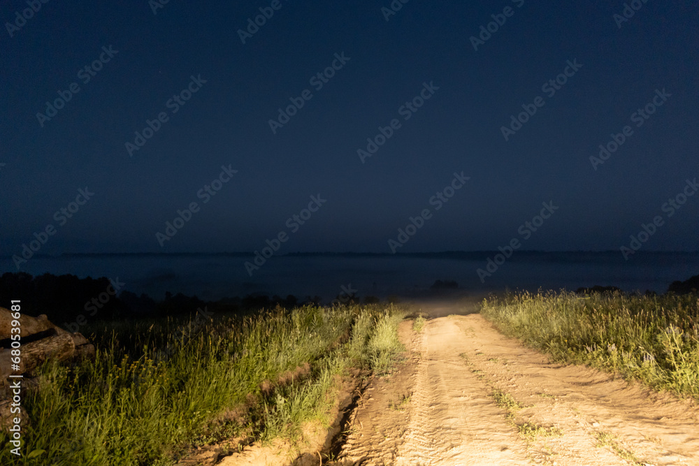 dry dirt road in the middle of nowhere lit with car headlights at early foggy morning dry dirt road in the middle of nowhere lit with car headlights at early foggy morning