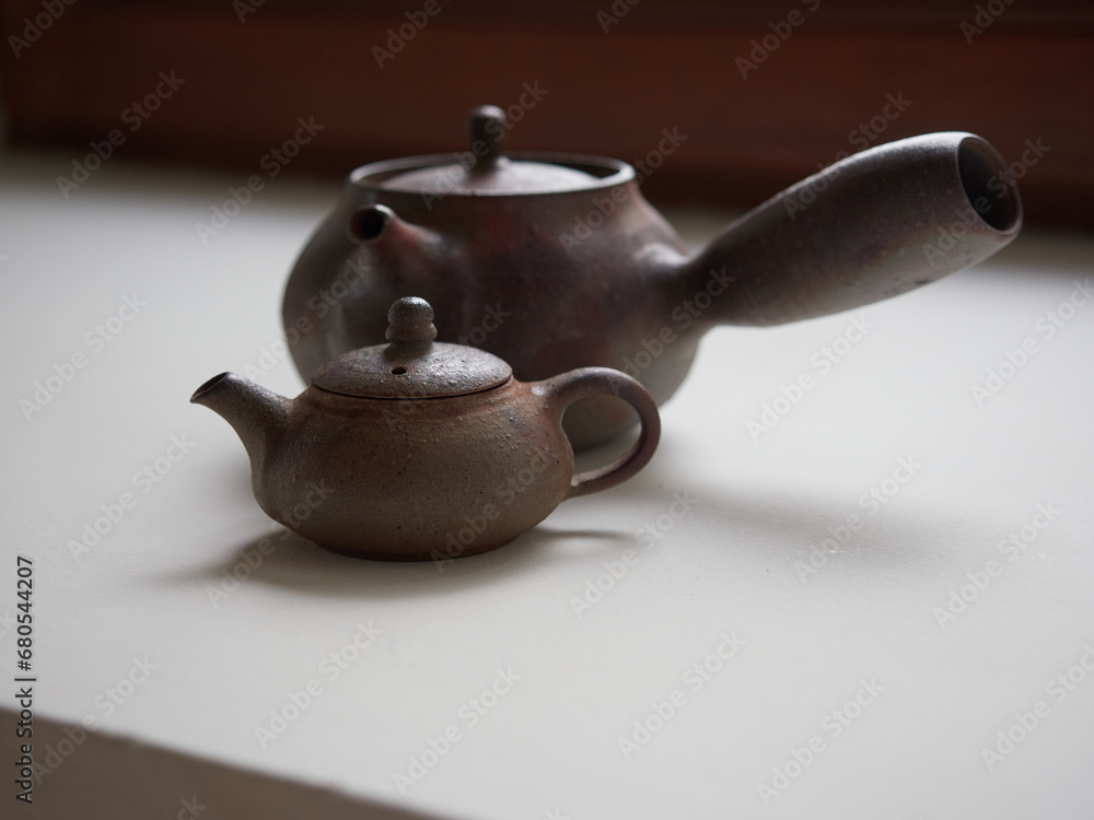 Small traditional Japanese brown clay teapot, behind it another one with a large side handle call 