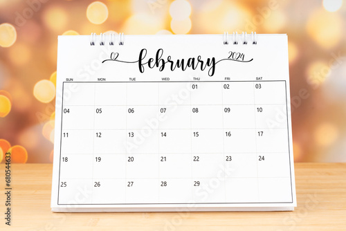 White February 2024 desk calendar on wooden table with gold light bokeh background.