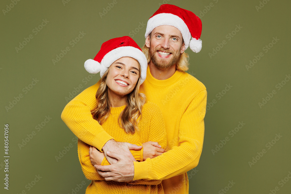 Merry young cheerful fun couple two friend man woman wear sweater Santa hat posing cuddle embrace look camera isolated on plain green background. Happy New Year celebration Christmas holiday concept. Merry young cheerful fun couple two friend man woman wear sweater Santa hat posing cuddle embrace look camera isolated on plain green background. Happy New Year celebration Christmas holiday concept.
