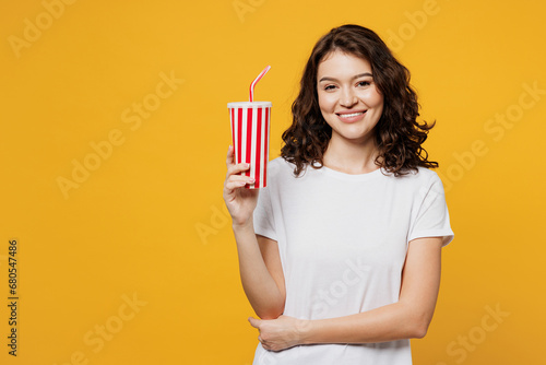 Young Caucasian cheerful woman she wear white blank t-shirt casual clothes hold in hand cup of soda pop cola fizzy water isolated on plain yellow orange background studio portrait. Lifestyle concept. photo