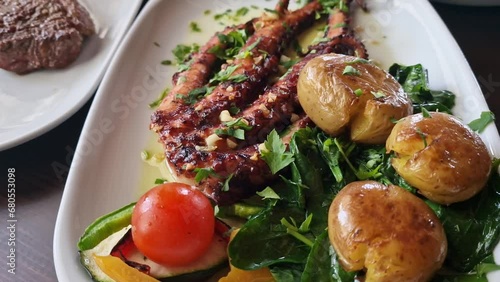 A traditional Portuguese dish of potato octopus with tomato and spinach called polvo a lagareiro close-up on a white plate photo