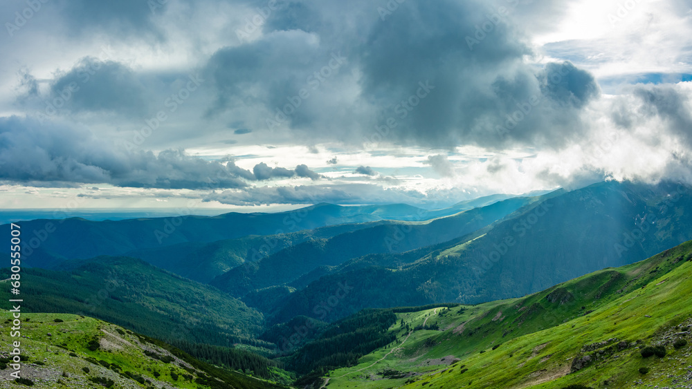 Sun shines through stormy clouds above Parang mountains. A dramatic sky can be seen as sun rays are penetrating the rainy clouds. Carpathian Massif, Romania.