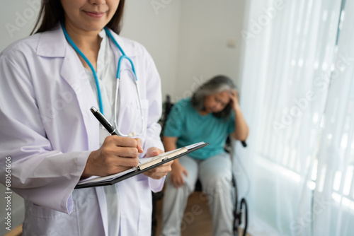 Doctor writing down the diagnosis on a clipboard after talking and Health check, Asian female elderly patient sitting in a wheelchair and has stress, to elderly, depression and health care concept.