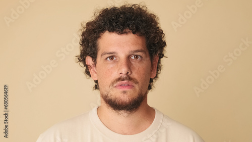 Bilde på lerret Close-up of an amazed guy with curly hair dressed in beige t-shirt looking at th