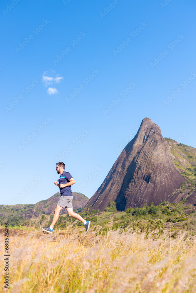 A man running outdoors against the backdrop of a towering rocky mountain. An image to inspire sports and wellness. Excellent for sports events campaigns