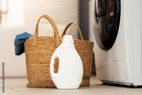 White bottle bottle laundry detergent, basket with clothes standing in laundry room. Mockup photo