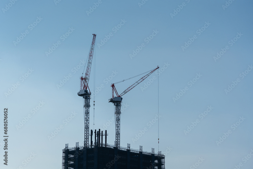 Silhouette of tower cranes machinery during building the high-rise condominium with clearly blue sky background. Construction industrial scene.