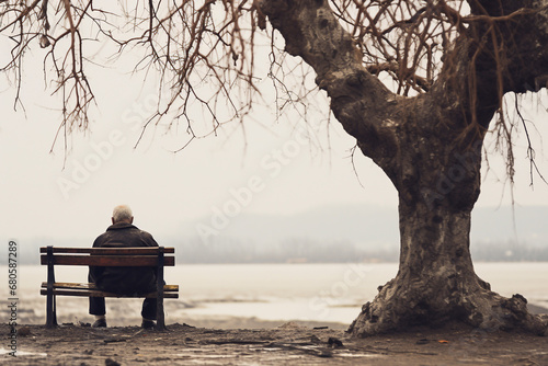 The elder is sitting alone on a bench. A lonely old man is sitting on a park bench.Elderly gentleman on a bench in contemplation. Lonely pensioner photo