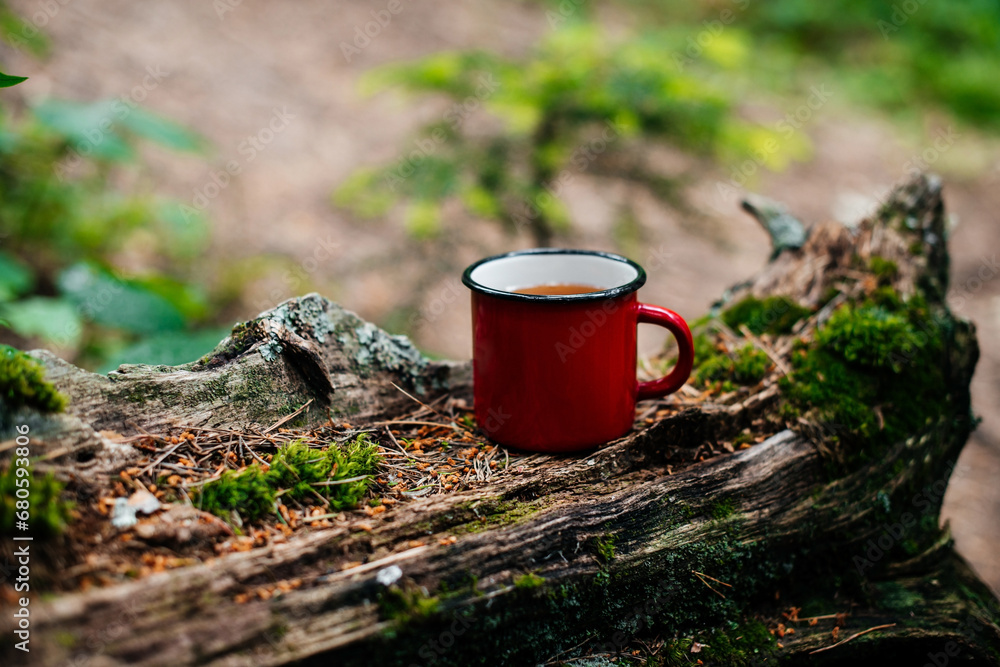 Obraz premium a red mug of tea stands on a log in the forest