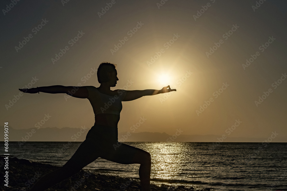 Woman performing warrior pose yoga on the beach at sunrise