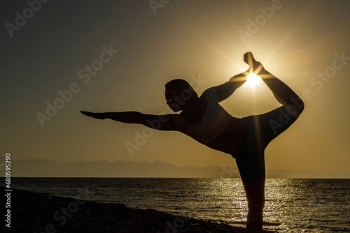 Young pretty woman performing Natarajasana yoga pose on the beach at sunset photo