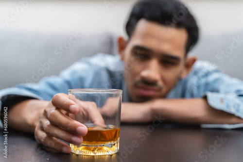 melancholy young Asian man drinks alcoholic whisky alone at home feeling dizzy after drunk photo