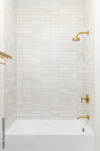 A shower and bathtub with brown subway tiles and a gold showerhead and faucet.